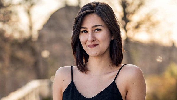 Young woman with dark shoulder-length hair smiling at camera outdoors during golden hour.