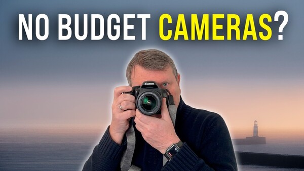 Photographer holding a DSLR camera up to his face against a coastal sunset backdrop.