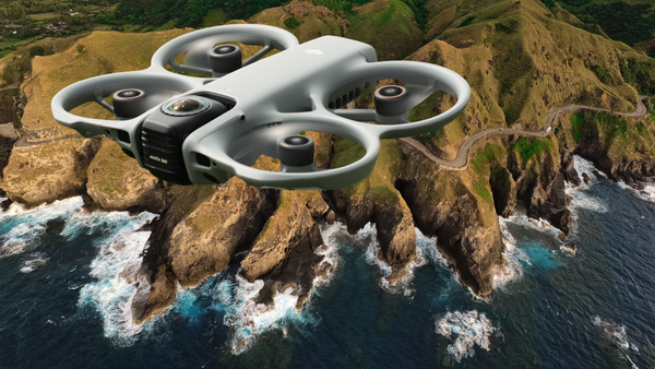 Quadcopter drone hovering above rocky coastal cliffs with crashing waves below.