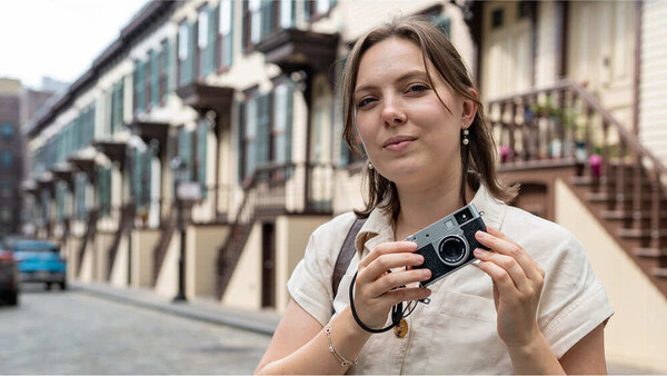Woman holding a vintage film camera on a European street lined with classical architecture