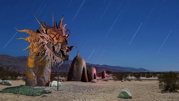 Large ornate wooden dragon sculpture in desert landscape with star trails visible in night sky