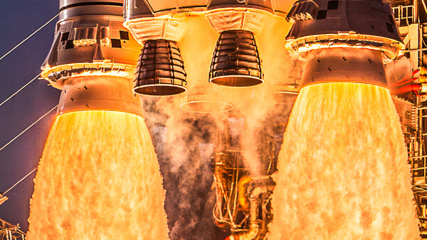 Space shuttle main engines igniting at night, producing bright yellow exhaust plumes against dark sky.