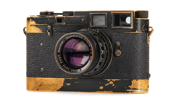 Weathered vintage rangefinder camera with worn brass trim and purple-tinted glass lens element.