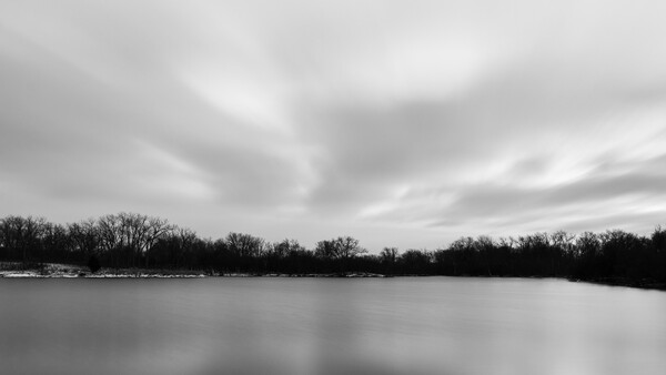 Frozen lake with bare trees along distant shoreline under overcast sky