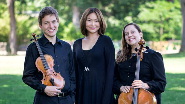 Three musicians in black clothing posing outdoors with violin and cello