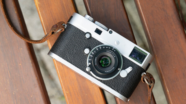 Vintage rangefinder camera with black leather body and brown leather strap on wooden surface.