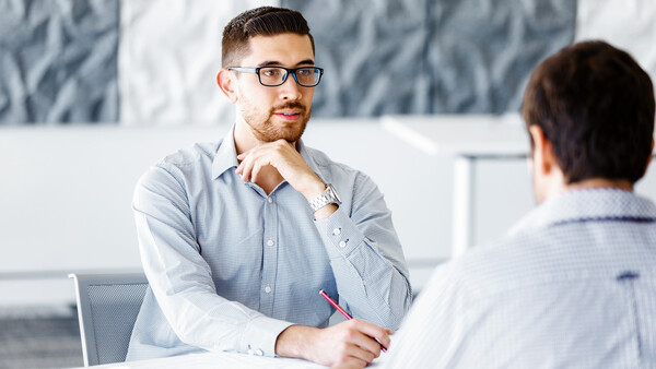 Two men in business casual clothing engaged in conversation at a table in a modern office setting.