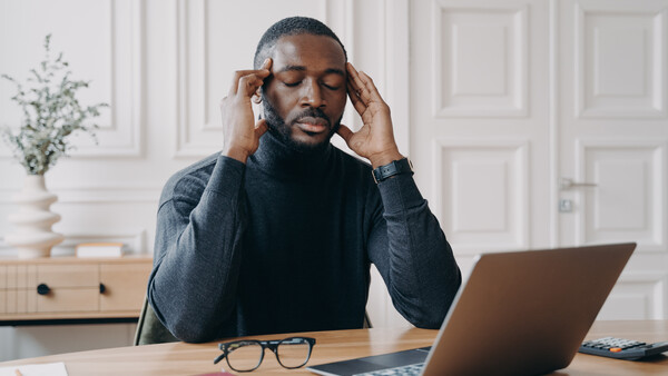 Man experiencing headache or stress while working at laptop at wooden desk.