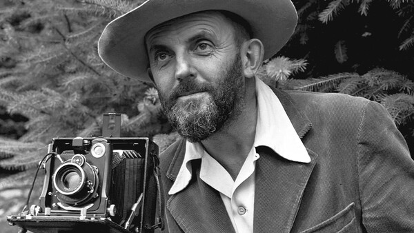 Bearded man in cowboy hat posing with a large format camera outdoors