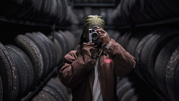 Photographer holding camera amid stacked black tires in industrial warehouse setting