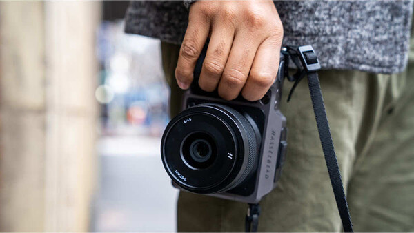 Photographer holding compact instant camera with gray fabric strap