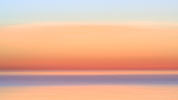 Serene seascape at sunset with calm, glassy water reflecting warm peachy-orange sky