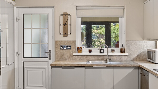 Modern kitchen with gray cabinetry, stone countertops, and garden views through large windows
