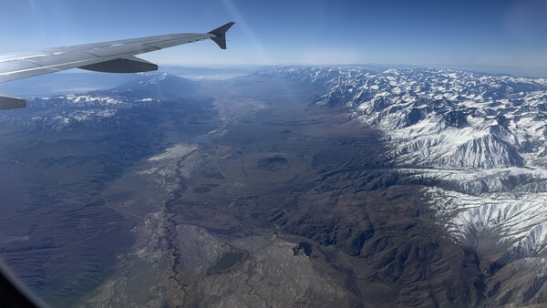 Aerial view from airplane window showing snow-capped mountain range and valleys below