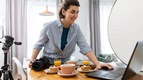 Female content creator at wooden desk with professional DSLR camera, ring light, and laptop during food photography setup