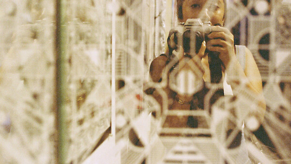 Photographer with camera reflected in mirror surrounded by reflective surfaces