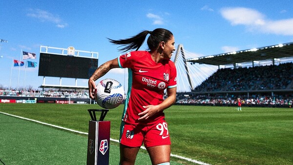 Female soccer player in red uniform holding ball at stadium sideline