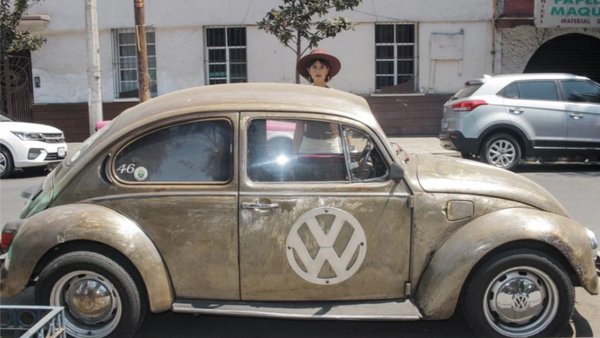 Vintage Volkswagen Beetle with patina finish and VW logo, driver visible through open window