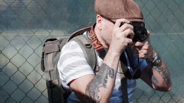 Photographer with camera and backpack shooting against chain-link fence