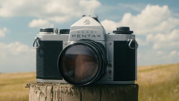 Pentax film camera mounted on wooden post in rural landscape