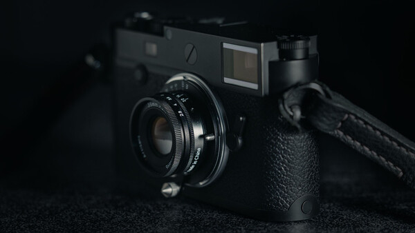 Black rangefinder camera with attached lens and shoulder strap on dark textured surface