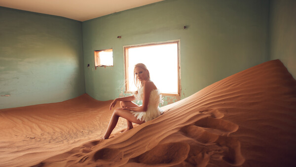 Woman posing on large sand dune inside minimalist room with green walls and bright doorway