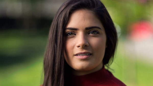 Portrait of a woman with long dark hair wearing a burgundy turtleneck against a blurred green background