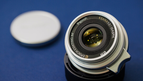 Vintage wide-angle lens with yellow-amber glass elements on blue background