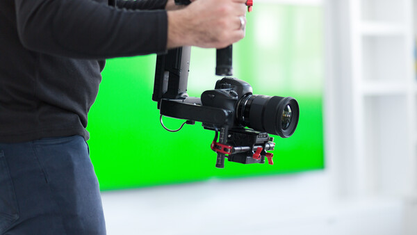 Cinematographer operating a gimbal-stabilized camera rig against a green screen