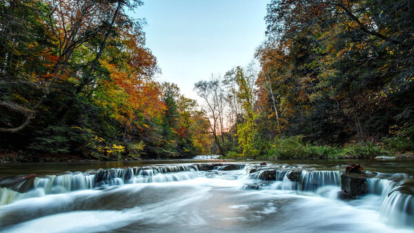Cascading waterfall flowing through autumn woodland with smooth long-exposure water effect