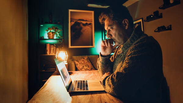 Man in yellow cardigan studying laptop at wooden desk surrounded by warm accent lighting