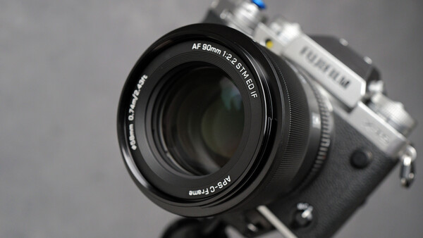 Fujifilm camera with AF 90mm f/2.4 R LM OIS lens mounted, shot against neutral gray background