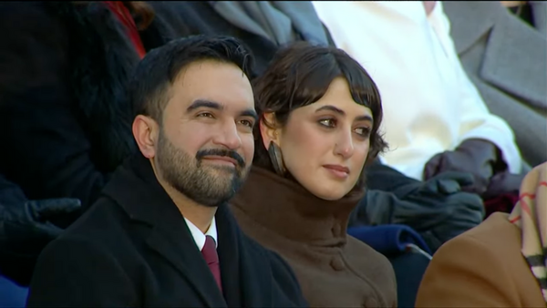 Man and woman sitting together outdoors, dressed in dark winter coats