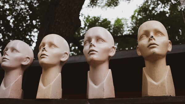 Four pale sculptural busts arranged in a row against a dark architectural element, looking upward