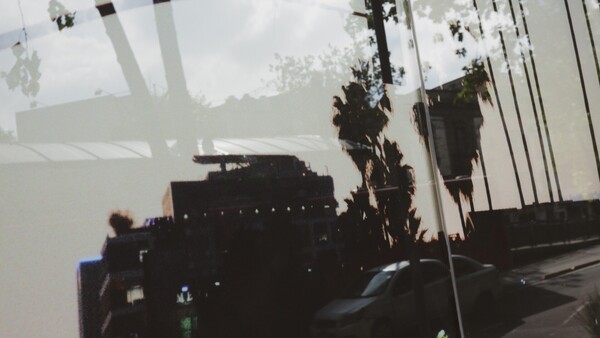 Double exposure of silhouetted buildings and palm trees overlaid with cloudy sky