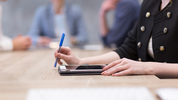 Woman taking notes with blue pen during professional meeting at wooden table