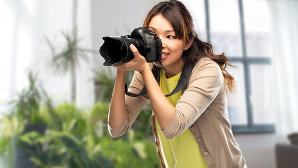 Woman holding a DSLR camera to her face, composing a shot in a bright interior space