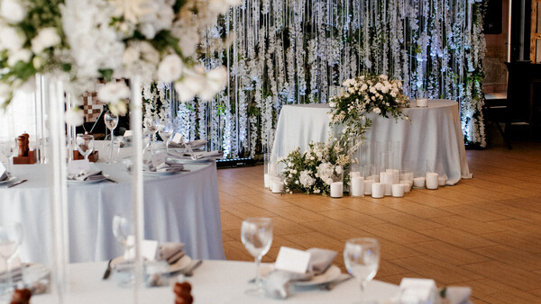 Elegant wedding reception setup with white linens, floral centerpieces, and cascading silver streamer backdrop