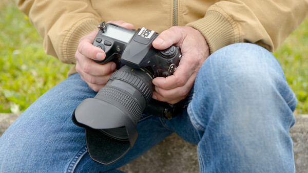 Photographer holding a DSLR camera with telephoto lens while sitting outdoors