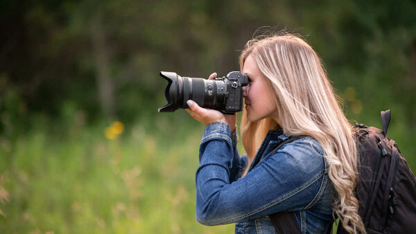 Female photographer with long blonde hair holding a DSLR camera with telephoto lens to her eye