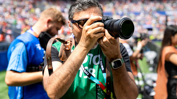 Sports photographer with telephoto lens at stadium event wearing green credential lanyard