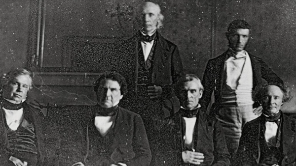 Five men in formal 19th-century attire arranged in a studio portrait