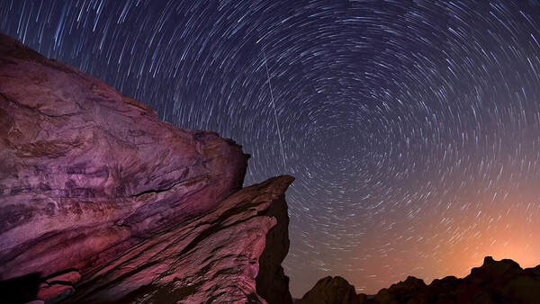 Star trail long exposure over illuminated desert rock formation at night