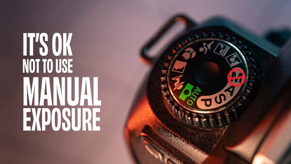 Close-up of a camera's exposure compensation dial with white text overlay reading 'IT'S OK NOT TO USE MANUAL EXPOSURE'