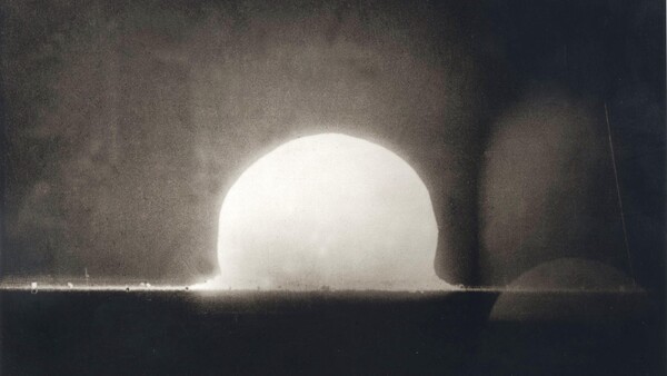 Nuclear explosion test shot showing bright hemispherical fireball rising above desert ground with shock wave and dust plume