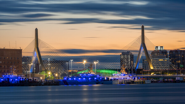 Illuminated cable-stayed bridge spanning dark water at twilight with city skyline and lit buildings