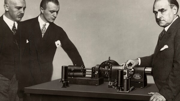Three men in business suits examine a large industrial machine on a table