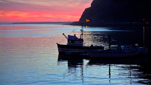 Fishing boat silhouetted at twilight in calm harbor waters with dramatic sunset sky