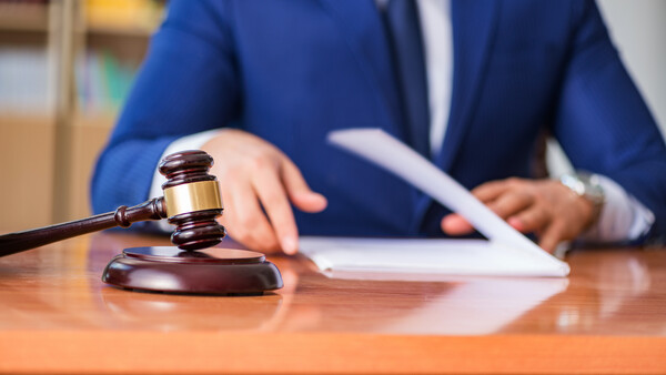 Lawyer in blue suit holding gavel at wooden desk with documents and tablet
