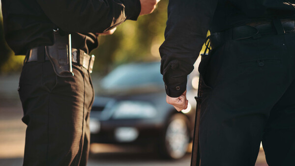 Two people in dark clothing shaking hands at night with blurred vehicles in background